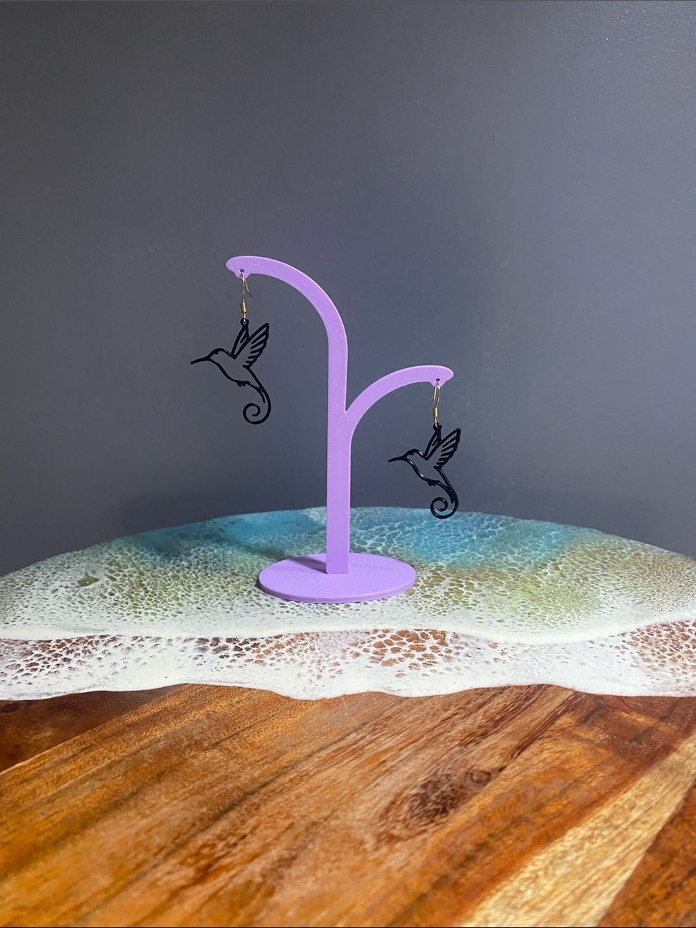 3D printed Black Hummingbird Drop Earrings on Purple Display